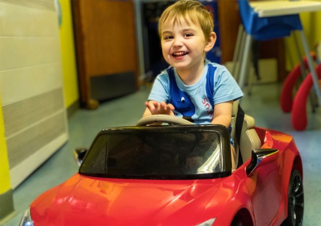 boy sitting in red toy car in hospital ward