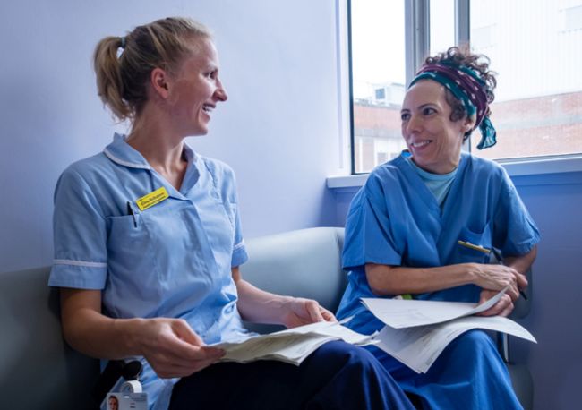 Two hospital staff smiling whilst having a conversation 