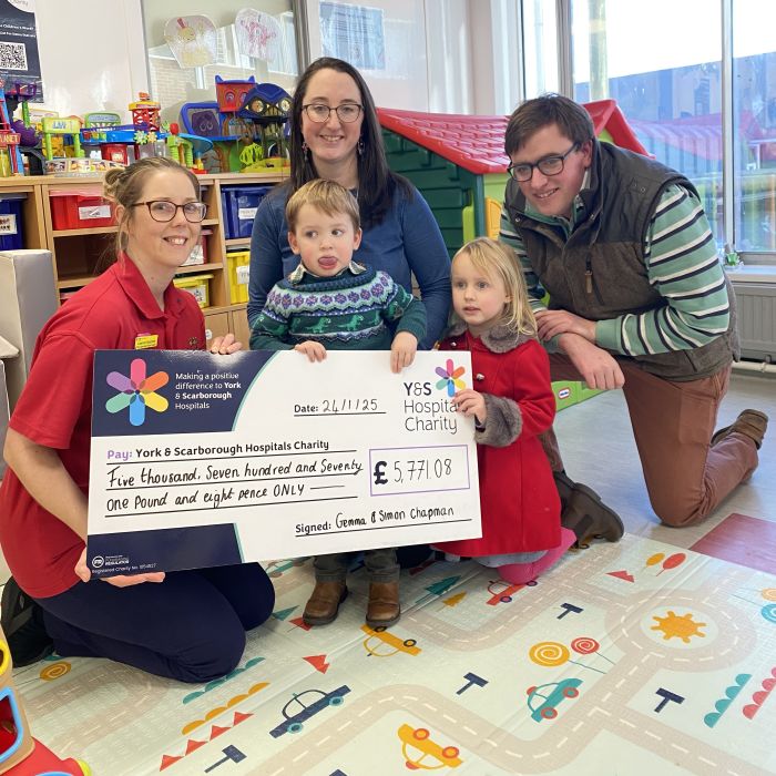 A family handing over a giant cheque to a play team member in York Hospital Children's Ward playroom