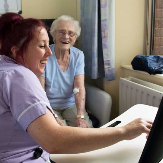 a nurse smiles as she treats a patient in a chair who is laughing 