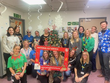 Staff wearing festive jumpers, smiling and holding charity logo board