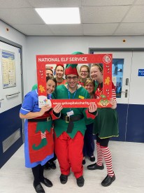 Staff dressed in festive clothing smiling with charity logo board