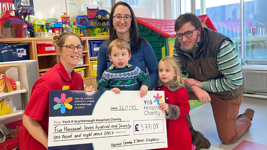 A family handing over a giant cheque to a play team member in York Hospital Children's Ward playroom